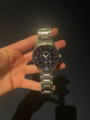 Citizen herrklocka i silver - Stilren klocka från Citizen med silverfärgad länk i metall och mörkblå urtavla. Klockan har flera små urtavlor och tydliga visare, vilket ger en sportig och modern look. Perfekt accessoar för dig som gillar klassisk design med en twist.