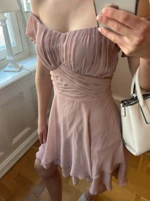 Ljusrosa offshoulder kortklänning - Söt ljusrosa kortklänning med offshoulder och plisserad överdel. Klänningen har ett omlottliknande liv och volangig kjol som ger en romantisk vibe. Perfekt för festligheter och fina sommardagar✨Ett statement-peice som är lätt att styla med accessoarer.