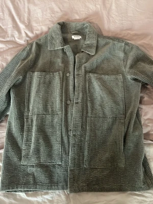 Grå overshirt i manchester från Weekday - Säljer en grå overshirt i manchestertyg från Weekday. Skjortan har två stora bröstfickor, klassisk krage och knäppning framtill. Perfekt lager-på-lager-plagg med avslappnad passform och cool struktur.