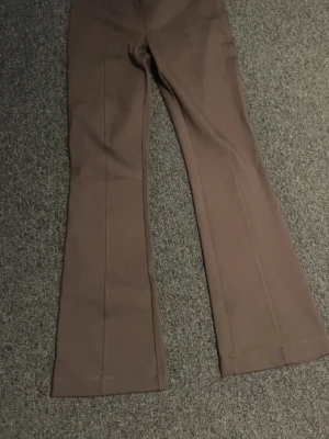 Bruna utsvängda kostymbyxor - Snygga bruna kostymbyxor med utsvängda ben och pressveck. Byxorna har två bakfickor med minimalistisk design. Perfekta för en stilren look och passar till många olika outfits.
