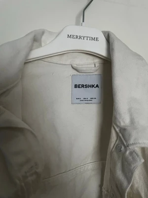 Vit jeansjacka från Bershka - Snygg vit jeansjacka från Bershka med klassisk krage, knäppning framtill och två bröstfickor med lock. Jackan har ett bälte i midjan för extra stil och passform. Perfekt för dig som vill ha en trendig och stilren look. Har använd bara en gång 