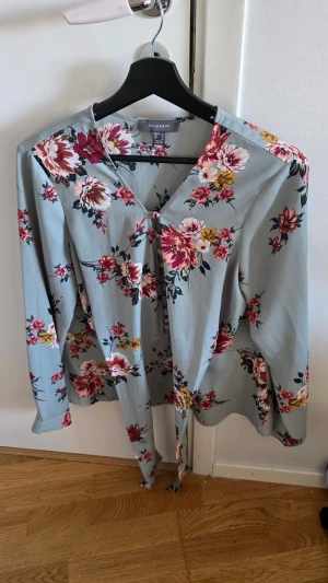 Blommig blus från Primark - Snygg blommig blus från Primark i ljusblått med rosa, röda och gula blommor. Blusen har långa ärmar, v-ringning och ett knytband framtill. Perfekt för dig som gillar en feminin och trendig stil.