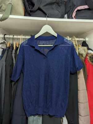 Mörkblå stickad kortärmad tröja - Snygg mörkblå stickad tröja med korta ärmar och krage. Tröjan har ett diskret hålmönster och är tillverkad i ett tunt, lätt material som ger en luftig känsla. Perfekt för lager-på-lager och stilrena outfits.