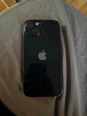Svart iPhone med dubbla kameror - Säljer en iPhone 14 (modell A2882) i färgen Midnight med 128 GB lagring. Telefonen har yttre skador men är fullt fungerande i övrigt. Perfekt för dig som fixar telefoner eller vill ha billiga reservdelar. Specifikationer & Skick: • Modell: iPhone 14, 128 GB. • Skärm: Sprickor samt en svart fläck (pixel-läckage) vid notchen. Touch fungerar. • Baksida: Glaset är spräckt (se bilder). • Batterihälsa: 80%. • Funktion: FaceID, kameror, laddning och högtalare fungerar utan problem. 