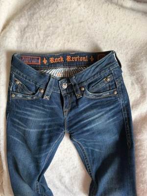 Blåa bootcut jeans från Rock Revival - Säljer ett par blåa bootcut jeans från Rock Revival. Jeansen har låg midja, slitningar framtill och super fin mörkblå färg. Tyvärr kommer inte jeansen till användning för mig❣️pris kan diskuteras 