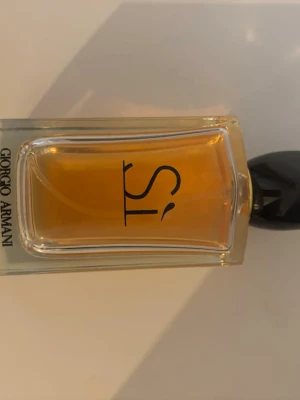 Giorgio Armani Sì Eau de Parfum - Giorgio Armani Sì Eau de Parfum med elegant rektangulär glasflaska och svart lock. Parfymen har en varm bärnstensfärgad vätska och stilren design med märkets logga på framsidan. Perfekt för dig som gillar lyxiga och feminina dofter.