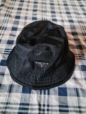 Svart bucket hat i tyg - Stilren svart bucket hat i mjukt tyg med klassisk form och bred brätte. Perfekt accessoar för en avslappnad streetstyle-look. Enkel att matcha med olika outfits och passar året runt.