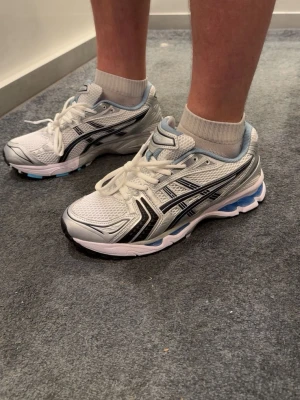 Asics gel kayano 14 - Snygga vita ASICS gel kayano 14 sneakers med svarta och silvriga detaljer samt blå inslag i sulan. Skrona är i storlek 44 men passar dig som har 43