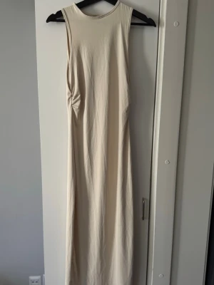 Beige ärmlös långklänning från SHEIN - Stilren beige långklänning från SHEIN med ärmlös design och rund halsringning. Klänningen har en lätt rynkning i sidan som ger en snygg detalj och markerar midjan. Tillverkad i ett mjukt och stretchigt material som sitter bekvämt på kroppen.