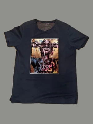 Mörkblå t-shirt Limitato Stop Wars - Cool mörkblå t-shirt från Limitato med ett stort färgstarkt tryck på bröstet och texten 'Stop Wars'. Skön passform och tillverkad i mjuk bomull. Perfekt för dig som vill sticka ut med ett statement-plagg.