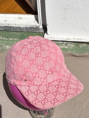 Rosa GG-keps - Säljer en rosa keps från  med det klassiska GG-mönstret över hela kepsen. Kepsen har böjd skärm och är tillverkad i ett slitstarkt tyg med ljus insida. Perfekt för dig som vill sticka ut med en lyxig accessoar.