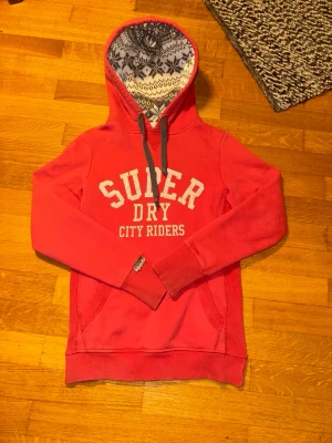 Superdry Hoodie - En riktigt fet röd vintage hoodie från Superdry 🤩Insidan av luvan är stickad i ett riktigt fett mönster, liknande snöflingor ❄️. En av de snyggaste superdry hoodies jag sett som passar perfekt för någon som gillar vintage👑. Storlek S men passar som XS. 