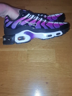 Nike Air Max Plus TN rosa/svart - Nike Air Max Plus TN sneakers med grymt snygg färgskiftning i rosa, lila och svart. Skorna har tydliga svarta linjer, vit sula med synliga Air Max-enheter och en liten silverfärgad swoosh på sidan. Ovandelen är i mesh för bra andningsförmåga och komfort.