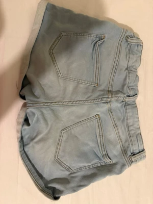 Ljusblå jeansshorts från Lindex - Säljer ett par ljusblå jeansshorts från Lindex med klassisk femficksdesign och uppvikta benslut. Shortsen har normal passform och stängs med dragkedja och knapp. Perfekta för varma dagar och enkla att matcha med olika toppar. Barnstorlek 154 men skulle säga att de passar xs