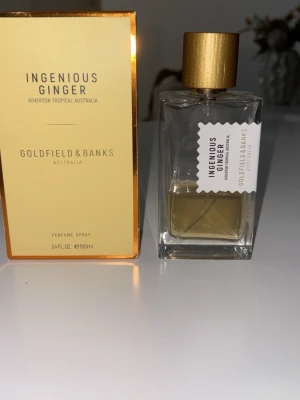 Goldfield & Banks Ingenious Ginger parfym - En exklusiv parfym från Goldfield & Banks, Ingenious Ginger. Flaskan är transparent med en guld-färgad kork och har en modern, stilren design. Doften är inspirerad av tropisk ingefära från Australien och kommer i en elegant förpackning med guldfärgade detaljer. Jag uppskattar ungefär 40 ml av 100 ml. Är även öppen för byte.