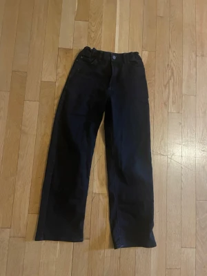 Svarta raka jeans från Lindex - Storlek 146. Snygga svarta jeans från Lindex med rak passform och klassisk femficksdesign. Jeansen har hög midja och stängs med knapp och dragkedja. Perfekta för en stilren och enkel look.