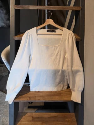 Vit ribbad topp från Lauren Ralph Lauren  - Trendig vit ribbad topp från LRL med fyrkantig ringning och puffiga långärmar. Tillverkad i ett mjukt, stretchigt material som ger en snygg passform. Perfekt att styla med jeans eller kjol för en clean look.