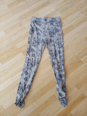 Mönstrade leggings från Röhnisch - Supersnygga leggings från Röhnisch med gråblått blommönster på ljus bakgrund och diskret bikakemönster. Stretchigt material och liten metallogo vid benslutet. Perfekta för dig som gillar unika detaljer och sportig stil. Står ingen storlek men skulle säga den passar S ja ha s