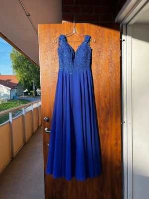Marinblå balklänning med spets - Elegant marinblå långklänning med vackert spetsliv och broderade detaljer upptill. Klänningen har breda axelband och ett flytande, svepande kjolparti. Perfekt för bal eller festliga tillfällen.