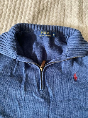 Blå stickad tröja Polo Ralph Lauren - Mysig blå stickad tröja från Polo Ralph Lauren. Tröjan har lång ärm, ribbstickade muddar och hög krage. Perfekt för lager på lager och enkel att matcha till olika outfits.