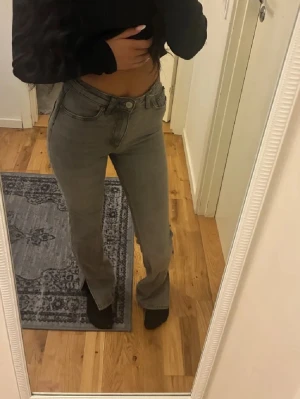 Bootcut jeans med slits  - Säljer ett par gråa jeans med hög midja och raka ben. Jeansen har klassiska fem fickor och stängs med knapp och dragkedja. Snygg tvätt och passar perfekt till en trendig vardagslook.