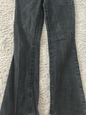 Svarta utsvängda jeans med fickor - Säljer ett par svarta jeans med utsvängda ben och stora fickor framtill med snygga silverknappar. Jeansen har en cool vintage vibe och passar perfekt till sneakers eller boots. Materialet är klassisk denim och färgen är tvättad svart.