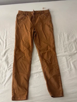 Bruna/orange slim fit jeans från Pulz - Snygga bruna jeans från Pulz i storlek 40. Modellen är slim fit med klassisk femficksdesign och knappgylf. Jeansen har en mjuk bomullskänsla och passar perfekt till en avslappnad stil. Enkla att matcha med både t-shirt och hoodie.