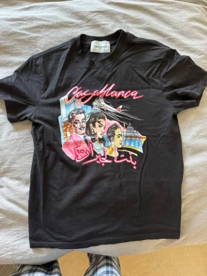 Svart Casablanca t-shirt - Snygg svart t-shirt från Casablanca med färgglatt grafiskt tryck framtill och texten 'Casablanca' i rosa. Klassisk passform med rund hals och korta ärmar. Perfekt för dig som vill sticka ut med en unik och trendig look.