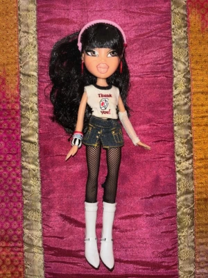 Vintage Bratz docka med original outfit & accessoarer – Y2K / tidigt 2000-tal - Säljer en original Bratz-docka från tidigt 2000-tal i mycket fint skick. Dockan har en klassisk Y2K-look med långt svart hår, stora ögon och komplett outfit med flera originalaccessoarer.  Outfiten består av topp, jeansshorts, nätleggings, vita boots, örhängen, armband och håraccessoar enligt bilderna. Dockan är välbevarad med fint hår och ansikte utan större skador.  Perfekt för samlare, nostalgiker eller dig som älskar Bratz och 2000-talsestetik.