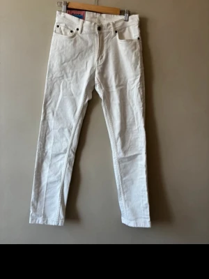 Vita raka jeans från Acne Studios - Säljer ett par vita jeans från Acne Studios i W29 L32 med rak passform och klassisk femficksdesign. Jeansen har bälteshällor, knappgylf och detaljer i metall. Perfekta för en clean och stilren look.