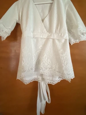 Vit spetsblus med knytband - Söt vit blus i spets med v-ringning och knytband i midjan. Blusen har trekvartsärm och fina broderade detaljer längs kanterna.Jag har sytt den själv så den har sina fel här och där❣️