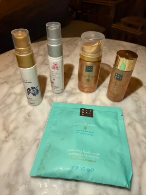 Blandade Rituals kroppsvårdsprodukter - Ett kit med olika kroppsvårdsprodukter från Rituals, inklusive två guldiga flaskor, två vita flaskor med pump och en turkos påse med body scrub. Produkterna har eleganta förpackningar i guld, vitt och turkos och innehåller bland annat Ritual of Karma och Ritual of Mehr.
