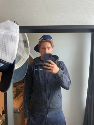 Mörkblå hoodie från Scotch & Soda - Snygg mörkblå hoodie från Scotch & Soda med dragkedja och huva. Tröjan har vit logga på bröstet och justerbara snören i huvan. Perfekt för en avslappnad och stilren look.