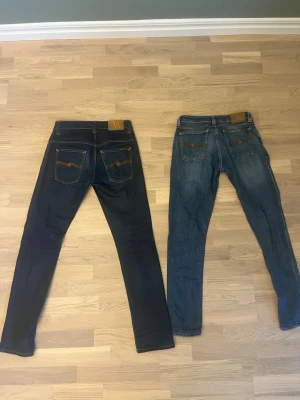 Mörkblå jeans från Nudie Jeans - Säljer två par mörkblå jeans från Nudie Jeans med klassisk orange söm och vågmönster på bakfickorna. Jeansen har rak passform och är tillverkade i denim med snygga detaljer. Perfekta för dig som gillar stilrena och tidlösa jeans. Ett par för 399kr två par för 699kr💸