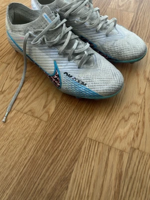 Nike Air Zoom vita fotbollsskor - Säljer ett par vita Nike Air Zoom fotbollsskor med blå och rosa detaljer. Använda men inga defekter eller skador på skorna. Skick 7/10. Köpta från Unisport för 3299kr. 