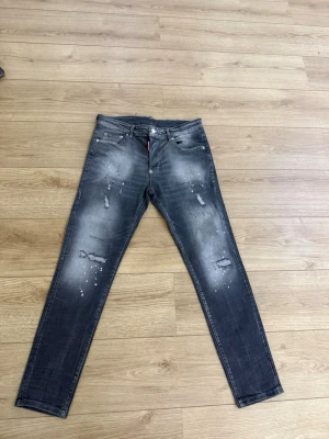 DSQUARED2 jeans - Snygga grå DSQUARED2 jeans med och slitna detaljer framtill. Jeansen har en tvättad look med spridda färgstänk och revor för en trendig streetstyle. Klassisk femficksmodell och knappgylf. Perfekta för dig som gillar en edgy stil.