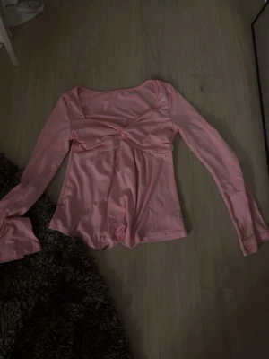 Rosa långärmad topp med twist - Trendig rosa topp med lång ärm och twistad detalj framtill. Toppen har en feminin passform med fyrkantig ringning och är tillverkad i ett mjukt material som känns skönt mot huden. Perfekt för att lyfta din outfit med en söt touch.