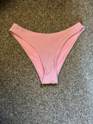 Rosa bikiniunderdel med glittereffekt - Snygg rosa bikiniunderdel med glittrig yta och klassisk trosaform. Perfekt för strand eller poolhäng. Materialet känns mjukt och stretchigt för en bekväm passform.
