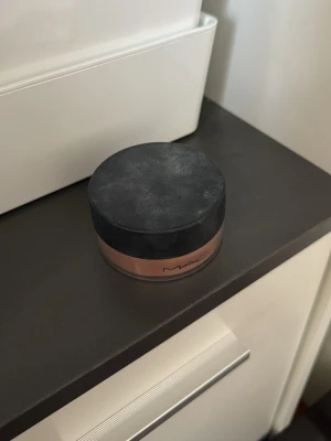 MAC löspuder foundation brun - Löspuder foundation från MAC i en brun nyans. Kommer i en rund burk med svart lock och transparent underdel så man ser färgen på pudret. Perfekt för att få en jämn och matt finish.
