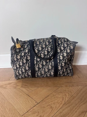 Dior bowling bag- mörkblå - Jättefin bowling bag från dior. Med det klassiska mörkblå och beiga monogrammet, mörklblåa läder detaljer och ett hänglås. Köpt på Vestiaire med authentication & quality control, därav garanterad äkthet. 30 cm i bredd, 25 cm hög/djup. Några små skavanker på sömmarna vid hörnen, annars i bra skick med precis nypreparerad dragkedja.