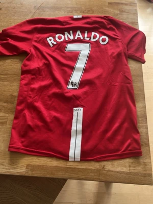 Manchester United Ronaldo matchtröja - Säljer en röd Manchester United matchtröja med Ronaldo och nummer 7 på ryggen. Tröjan har Champions League-märke på ärmen, AIG som sponsor och Nike-logga framtill. Materialet är lätt och andas, perfekt för fotboll eller samling.