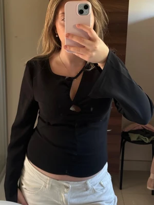 Svart långärmad topp från Bik Bok - Stilren svart långärmad topp från Bik Bok med croppad passform och snygg twistad detalj framtill. Tillverkad i ett mjukt, lätt material som ger en clean look. Perfekt att matcha med jeans eller kjol.