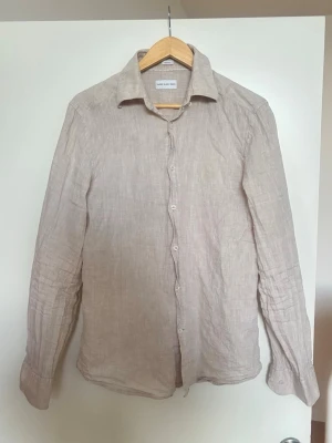 Beige linneskjorta från Samsøe Samsøe - Stilren beige skjorta i linne från These Glory Days. Skjortan har klassisk krage, knäppning framtill och långa ärmar. Perfekt för en avslappnad men ändå snygg look under varmare dagar. 100% linne