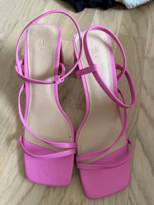 Rosa strappy pumps från H&M - Snygga rosa pumps från H&M med tunna remmar och fyrkantig tå. Skorna har en blockklack och öppen design som ger en trendig vibe. Tillverkade i syntetmaterial med justerbar ankelrem för extra komfort.