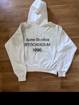 Vit hoodie från Acne Studios - Säljer en stilren vit hoodie från Acne Studios med klassisk huva och ribbade muddar. Hoodien är tillverkad i mjukt material och har en avslappnad passform. Perfekt för en clean och modern look.