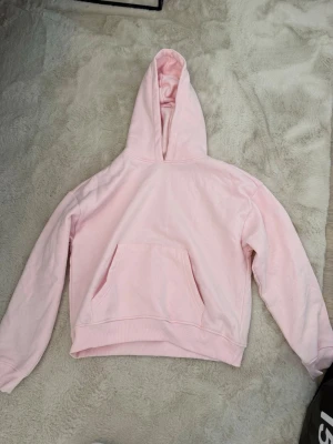 Ljusrosa hoodie med magficka - Säljer en ljusrosa hoodie med klassisk huva och stor magficka framtill. Hoodien har ribbade muddar vid ärmslut och nederkant.