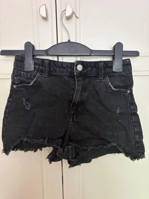Svarta jeans shorts - Säljer ett par svarta jeansshorts från H&M med hög midja och fransig kant. Shortsen har slitna detaljer och klassiska fem fickor. Perfekta för sommarens alla äventyr och ger en cool vibe till din outfit.