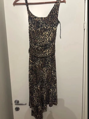 Leopardmönstrad långklänning Tiana B. - Snygg långklänning från Tiana B. i leopardmönster med smala axelband och figurnära passform. Klänningen har en mjuk och stretchig känsla, perfekt för dig som vill sticka ut. Färgerna går i beige, svart och brunt.