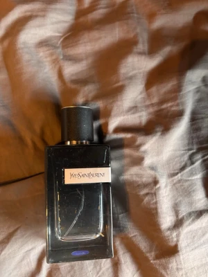 YSL Y EDP 100 ML - Snygg parfymflaska från Yves Saint Laurent i svart glas med metallock och tydlig logotyp på framsidan. Flaskan har en stilren, rektangulär form och känns lyxig och modern. Perfekt för dig som gillar exklusiva dofter och elegant design. Använt ungefär hälften av denna, tröttnat på doften och vill sälja till någon som kommer använda den mer än mig, priset går att diskutera 