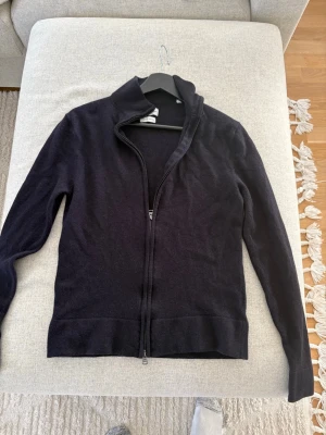   Merinoullströja (Full zip) från These Glory Days - Säljer en svart tröja i merinoull från These Glory Days. Tröjan har dragkedja framtill, hög krage och är tillverkad i Superior Merino. Perfekt för dig som gillar stilrena och bekväma plagg med en klassisk look. Storlek S men sitter mer som XS